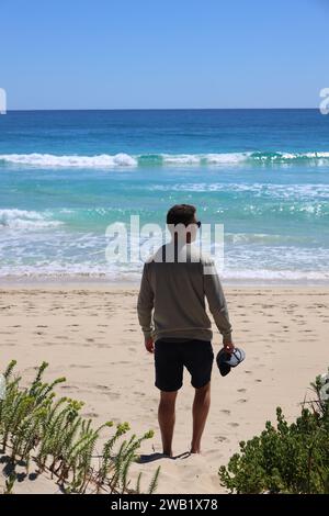 Ein einsamer Mann, der am Ufer eines Strandes steht und auf die Weite des Meeres blickt Stockfoto