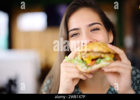 Glückliche Frau isst Burger und sieht dich in einem Restaurant an Stockfoto