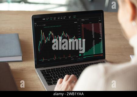 Laptop-Bildschirmansicht mit Aktiendiagrammen, Grafiken über weiblicher Schulter Stockfoto