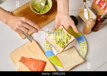 Blick von oben auf die Hände einer Frau, die zerpürierte Avocado auf Toast verteilt Stockfoto