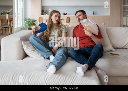 Familie Ehefrau, Ehemann leidet unter Verstopfungen und winkt zu Hause blaues Papier. Sommer heißes Wetter Stockfoto