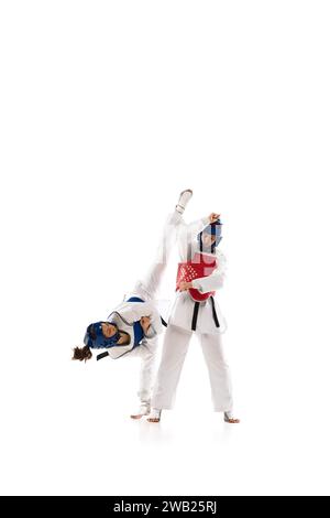 Zwei junge Mädchen im Dobok- und Helmtraining, üben Taekwondo-Posen, Haltungen isoliert über weißem Hintergrund Stockfoto