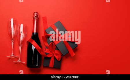 Champagner und Geschenk: Feierliches Duo auf rotem Hintergrund mit Textfeld. Grußkarte zum Valentinstag Stockfoto