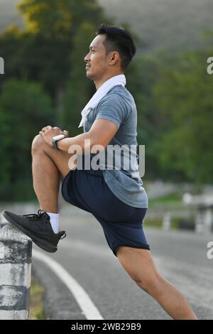 Porträt eines motivierten männlichen Athleten, der vor dem Laufen im Park Beine streckt. Aktives Lifestyle-Konzept Stockfoto