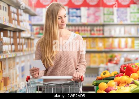 Attraktive junge Frau schiebt einen Einkaufswagen und kauft Lebensmittel im Supermarkt Stockfoto