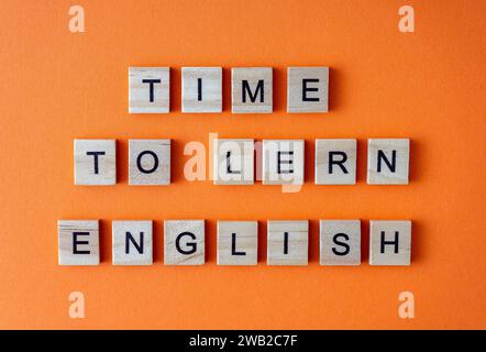 Zeit, Englisch zu lernen. Motivation. Der Satz ist in Holzbuchstaben von oben angeordnet. Motivation. Orangefarbener flacher Lay-Hintergrund Stockfoto