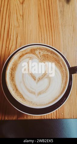 Dekorative Kaffeetasse mit Latte in dunklem Design auf Holztisch Stockfoto