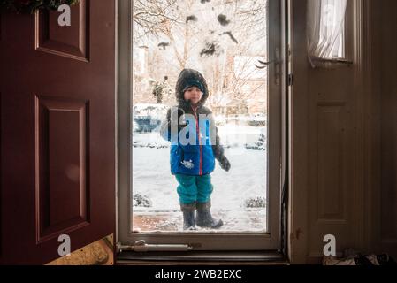 Vorschulkinder in Schneebekleidung stehen an verschneiten Tagen vor der Sturmtür Stockfoto