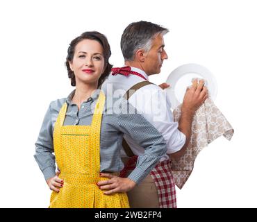 Lächelnd starke Frau, die gerade ihren Mann in Schürze Reinigung Geschirr Stockfoto