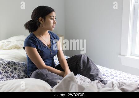 Birassisches Teenager-Mädchen sitzt auf einem ungebauten Bett und sieht deprimiert aus Stockfoto