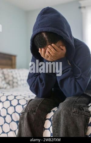 Birassisches Teenager-Mädchen sitzt auf dem Bett mit dem Kopf in den Händen und sieht deprimiert aus Stockfoto