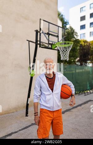 Senior-Mann spielt draußen Basketball auf dem Basketballfeld in der Stadt. Ein älterer, vitaler Mann hat einen aktiven Lebensstil und macht jeden Tag Sport. Stockfoto