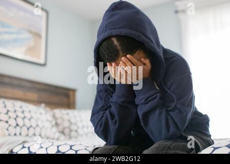 Birassisches Teenager-Mädchen sitzt auf dem Bett mit dem Kopf in den Händen und sieht deprimiert aus Stockfoto