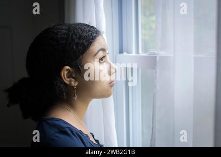 Birassisches Teenager-Mädchen schaut mit ernstem Ausdruck aus dem Fenster Stockfoto