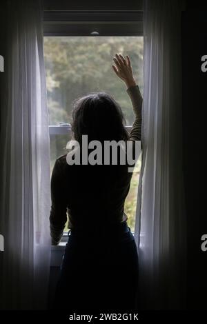 Eine ältere weiße Frau in Silhouette schaut aus dem Fenster Stockfoto