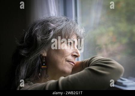 Eine ältere weiße Frau im Profil sieht deprimiert aus dem Fenster aus Stockfoto