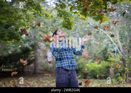 Birassisches Teenager-Mädchen, das Herbstblätter übergibt und lacht Stockfoto