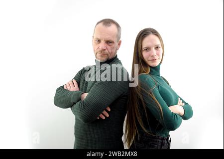 Ein Mann und eine Frau auf weißem Hintergrund, die bei einem Fotoshooting im Studio posieren, drücken sich den Rücken zueinander, glätten ihr Haar und schlagen einen selbstbewussten Look. Grüne Kleidung, ein paar Leute Stockfoto