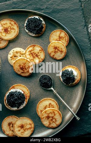 Blinis mit schwarzem Kaviar und Frischkäse, von oben geschossen, Mini-Pfannkuchen, eine elegante Vorspeise Stockfoto