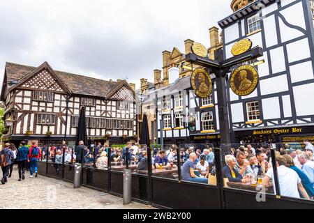 Menschen, die im Biergarten des denkmalgeschützten Old Wellington Pubs trinken, erbaut 1552 in Manchester, England Stockfoto