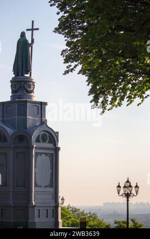 Historisches Denkmal des Heiligen Wladimir mit Kreuz gegen Sommer Kiew. Statue des Heiligen Volodymyr mit Baum und Straßenlaterne im Morgengrauen. Stockfoto