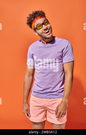 Aufgeregter junger afroamerikanischer Mann in Brille und lässiger Kleidung auf orangem Hintergrund, Mann Stockfoto