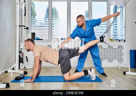 Erfahrener Physiotherapeut, der beim Training des Mannes während der Genesungssitzung im Fitnessstudio des kinesio-Zentrums hilft Stockfoto