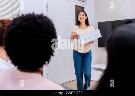 Glückliche Frau, die den Gästen Pizzaboxen bei einem freundlichen Treffen anbietet. Stockfoto