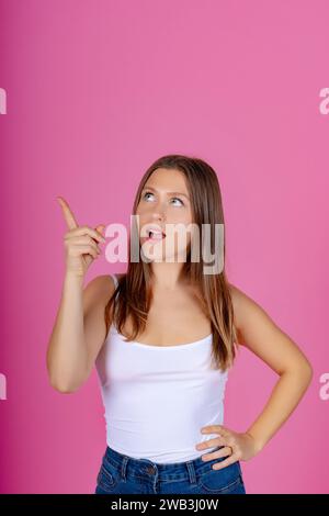 Ein junges Weibchen in weißer Spitze, das nach oben zeigt, Ausdruck einer neuen Idee, rosa Hintergrund. Stockfoto