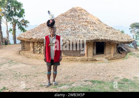 Ältester aus dem Stamm der Konyak in traditioneller zeremonieller Kleidung, vor einem hölzernen Konyak-Haus, dekoriert mit Stierschädeln, Nagaland, Indien Stockfoto