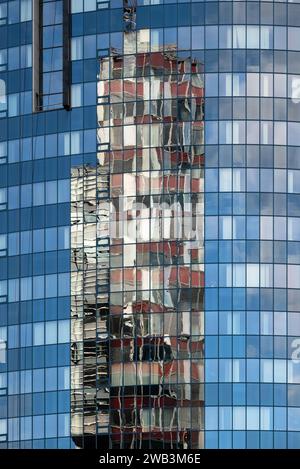 Das Foto zeigt eine Nahaufnahme der Fassade eines Glashochhauses. Die glatte, reflektierende Oberfläche des Gebäudes erfasst ein verzerrtes Bild eines Stockfoto