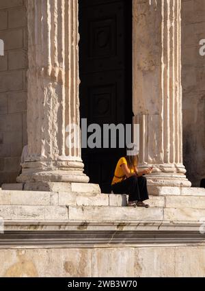 Nimes, Frankreich - 4. oktober 2023: Junge Dame sitzt zwischen den Säulen des römischen Tempels Maison Carree in der Stadt Nimes in Südfrankreich Stockfoto