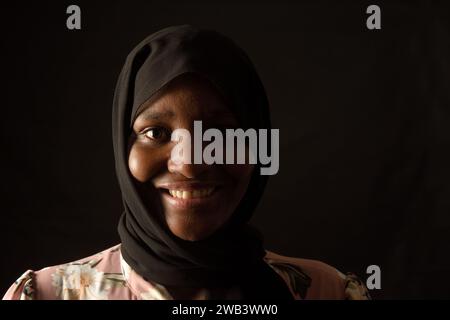 Porträt einer afrikanerin, die auf schwarzem Hintergrund lächelt Stockfoto