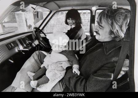 Kenneth MacMillan und Deborah MacMillan und das neue Baby Charlotte im Auto vor ihrem Haus in Wandsworth. Kenneth MacMillan war ein britischer Balletttänzer und Choreograf und künstlerischer Leiter des Royal Ballet in London. 1973 arbeitete er an Manon, einem Ballett mit drei Akten, als künstlerischer Leiter. Deborah MacMillan war eine Künstlerin, die Ballette für die Bühne und das Fernsehen entworfen hat. Wandsworth, London, England, 1970er Jahre Großbritannien HOMER SYKES Stockfoto