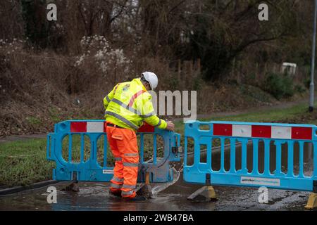 Horton, Wraysbury, Berkshire, Großbritannien. Januar 2024. Ein Mann aus dem Royal Borough of Windsor & Maidenhead errichtet Barrieren, um eine Straße wegen Überschwemmungen in Horton, Wraysbury Berkshire, zu schließen. Die Themse ist über die Ufer geplatzt und es gibt eine Reihe von Straßensperren in der Umgebung. Quelle: Maureen McLean/Alamy Live News Stockfoto