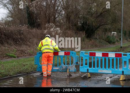 Horton, Wraysbury, Berkshire, Großbritannien. Januar 2024. Ein Mann aus dem Royal Borough of Windsor & Maidenhead errichtet Barrieren, um eine Straße wegen Überschwemmungen in Horton, Wraysbury Berkshire, zu schließen. Die Themse ist über die Ufer geplatzt und es gibt eine Reihe von Straßensperren in der Umgebung. Quelle: Maureen McLean/Alamy Live News Stockfoto