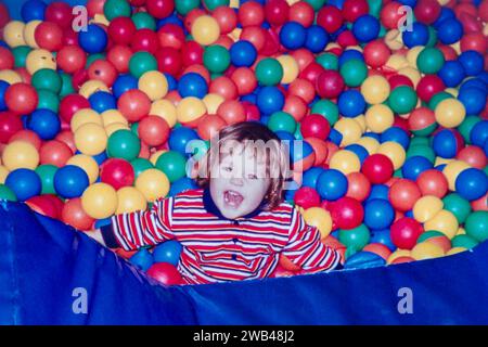 Archivfoto von 1994. Ein kleines Mädchen, das in der Ballgrube spielt und Spaß beim Spielen mit bunten Bällen hat. Stockfoto