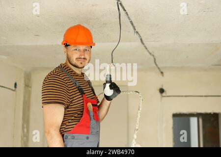 Elektrisch in einheitlichen Schutzhandschuhen und Schutzhelm, Prüfung und Messung der elektrischen Spannung in der Glühlampe mit einem Prüfschraubendreher. Ex Stockfoto