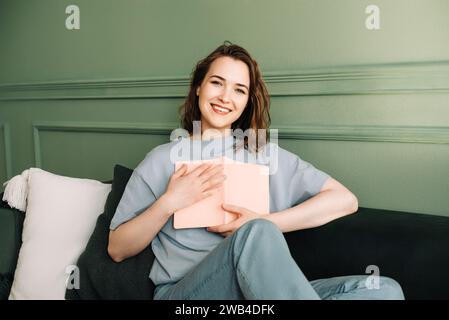 Freudige Frau mittleren Alters, die ein Buch schließt. Lächelnde Dame, die ein Buch mit fröhlichem Ausdruck umschließt. Glück und literarische Verbindung. Mitte Stockfoto