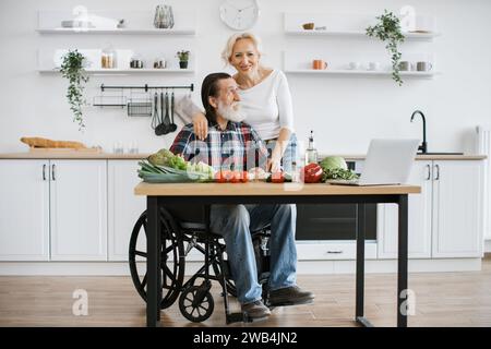 Behinderter Mann mit grauem Bart und Frau, die gesunden Gemüsesalat zubereiten. Stockfoto