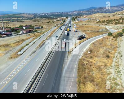 Blick von oben auf eine Asphaltstraße mit Lastwagen, Felder, Berge in der Nähe der Stadt an einem sonnigen Tag, Türkei. Stockfoto