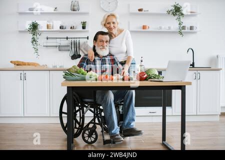 Behinderter Mann mit grauem Bart und Frau, die gesunden Gemüsesalat zubereiten. Stockfoto