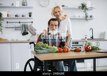 Behinderter Mann mit grauem Bart und Frau, die gesunden Gemüsesalat zubereiten. Stockfoto