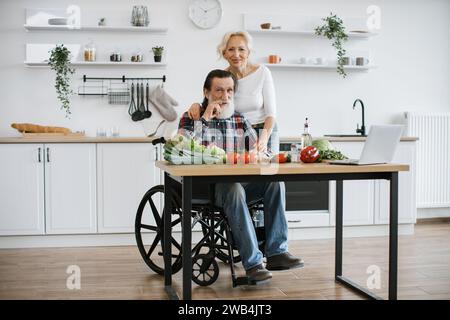Behinderter Mann mit grauem Bart und Frau, die gesunden Gemüsesalat zubereiten. Stockfoto