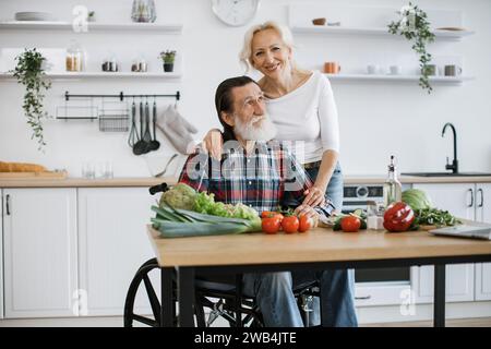 Behinderter Mann mit grauem Bart und Frau, die gesunden Gemüsesalat zubereiten. Stockfoto