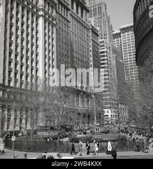 1960er Jahre, historisch, Manhattan, New York, USA. Sie zeigen die hohen Gebäude und Skyscapers, die das berühmte finanische Viertel dominieren, und einen umzäunten öffentlichen Park oder Gartenbereich mit Statuen, in denen die Menschen sitzen. Stockfoto