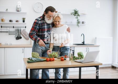 Das alte kaukasische Paar verbringt Zeit zur freien Verfügung, um in der modernen hellen Küche Frühstück zu kochen. Stockfoto