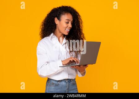 Glückliche afroamerikanerin, die ihren Laptop benutzt, gelber Hintergrund Stockfoto