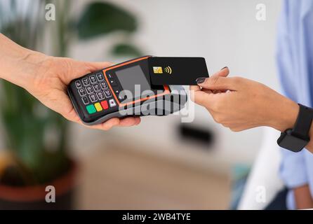 Die Hände der Dame halten die schwarze kontaktlose Kreditkarte über den Kartenleser, um die Zahlung abzuschließen Stockfoto