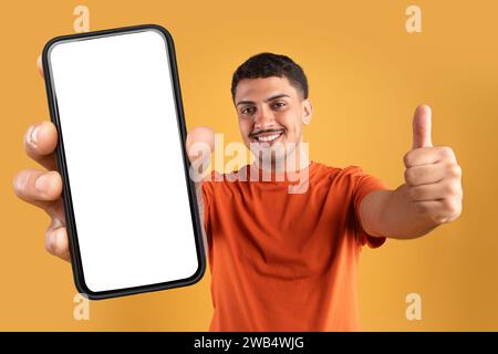 Fröhlicher brasilianischer Mann, der ein riesiges Handy mit weißem Bildschirm hält Stockfoto